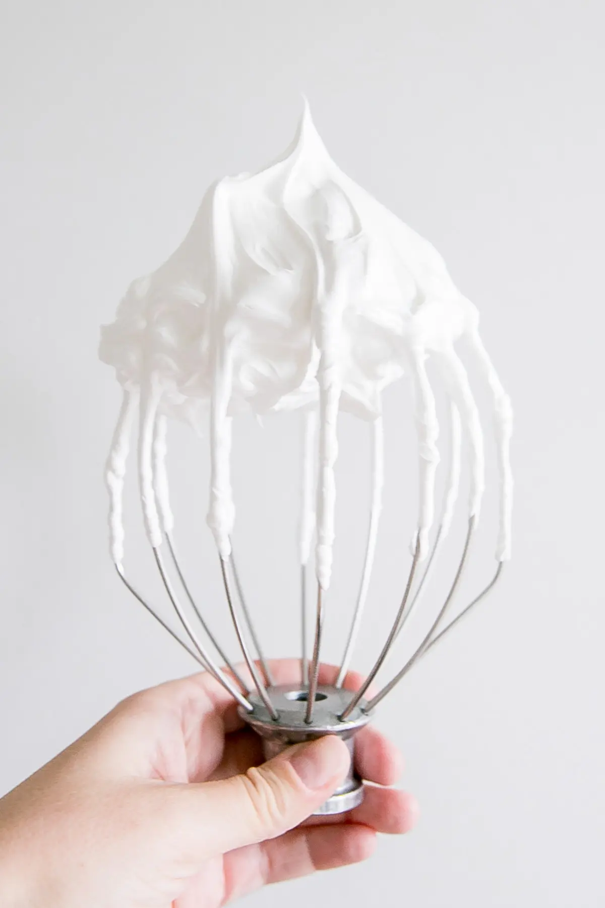 This old-fashioned 7 minute frosting recipe is light, delicious, and easy to make. A pure white frosting that's perfect for a variety of delicious desserts. | livforcake.com Holding a stand mixer whisk showing a stiff peak meringue.