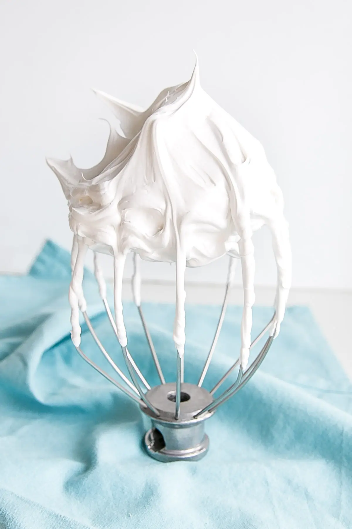 This old-fashioned 7 minute frosting recipe is light, delicious, and easy to make. A pure white frosting that's perfect for a variety of delicious desserts. | livforcake.com Seven minute frosting on a stand mixer whisk on a blue cloth.