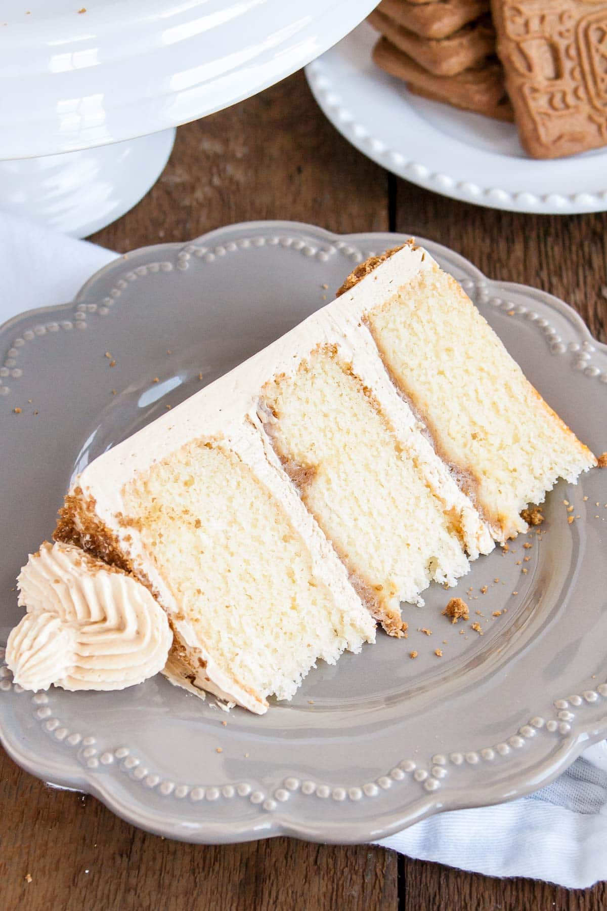 This Biscoff Cake pairs fluffy vanilla cake layers with a sweet cookie butter frosting and crushed speculoos cookies. | livforcake.com Slice of biscoff cake on a plate showing the layers of crunchy cookie butter.