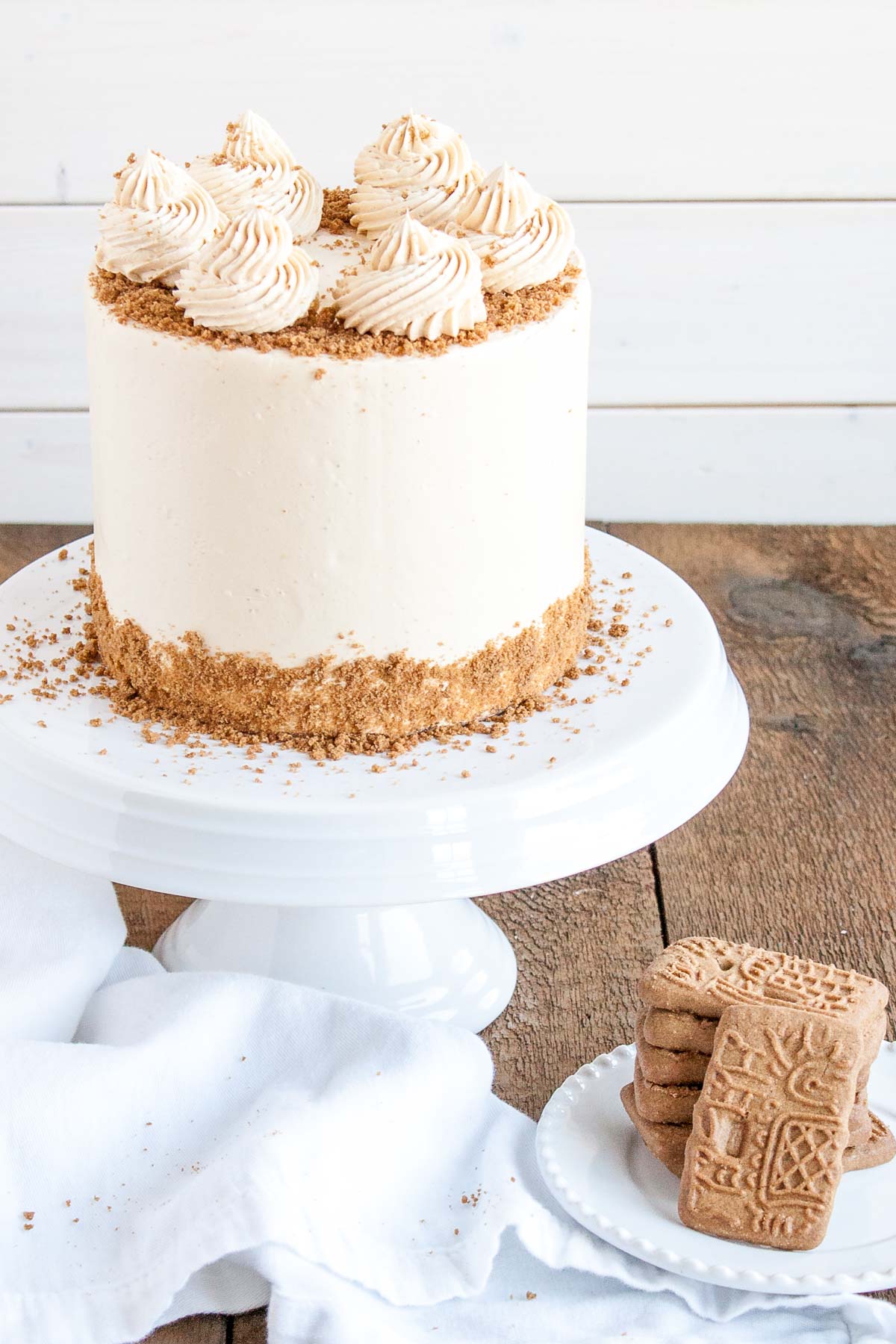 This Biscoff Cake pairs fluffy vanilla cake layers with a sweet cookie butter frosting and crushed speculoos cookies. | livforcake.com Angled shot of the biscoff cake with speculoos cookies on a plate beside it.