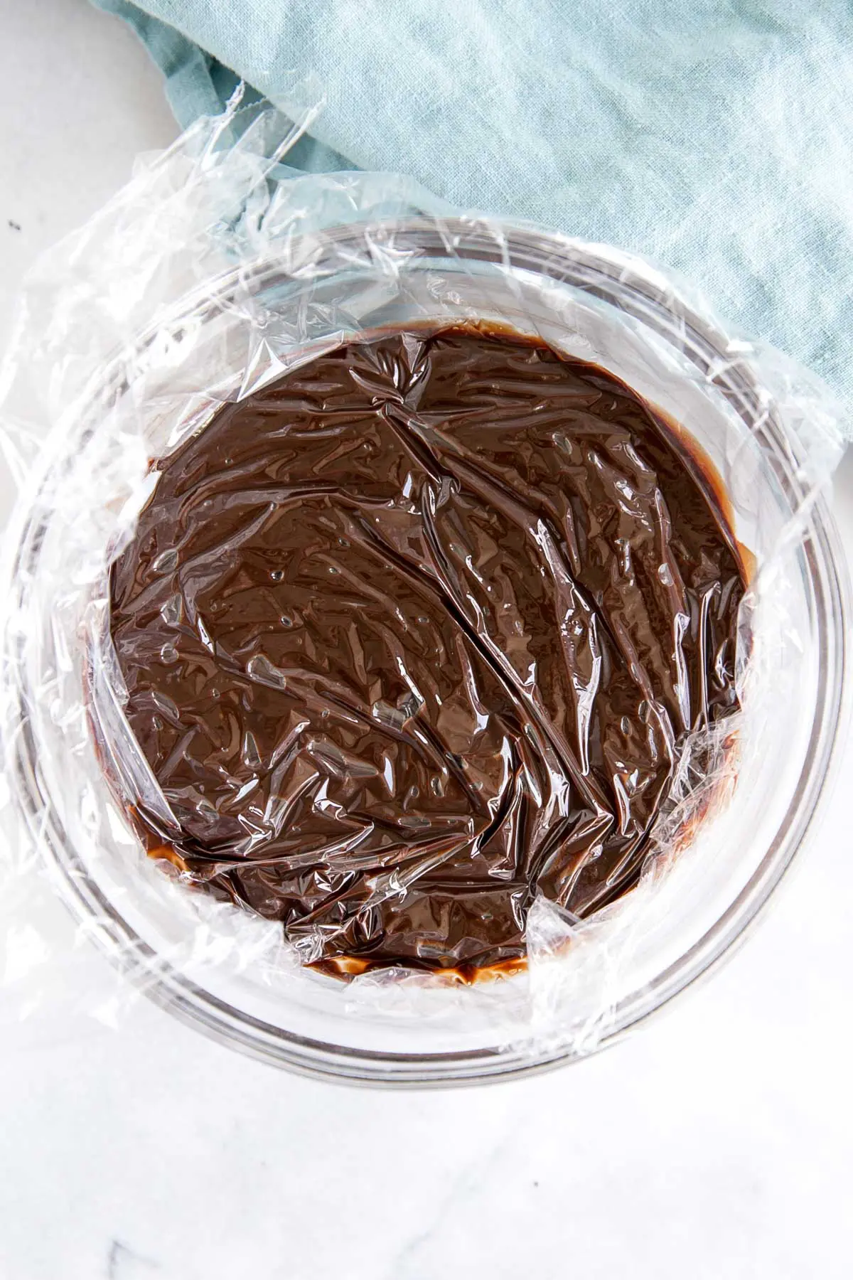 How to make Chocolate Ganache! A simple, two-ingredient recipe for a delicious frosting, filling, drip, or glaze. | livforcake.com Ganache in a bowl with plastic wrap directly on top.