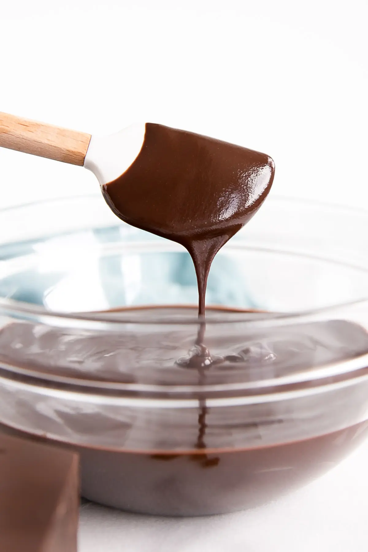 How to make Chocolate Ganache! A simple, two-ingredient recipe for a delicious frosting, filling, drip, or glaze. | livforcake.com Dark chocolate ganache drizzling off a white spatula into a bowl.