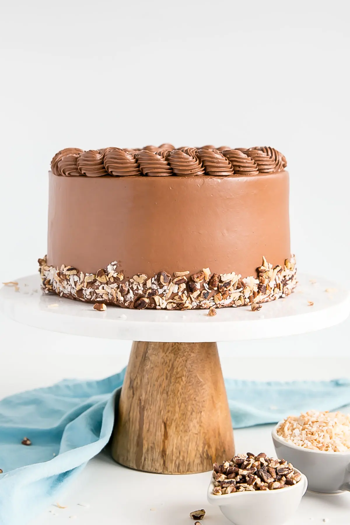This Classic German Chocolate Cake combines rich chocolate cake layers with a sweet coconut pecan filling and a dreamy chocolate buttercream. | livforcake.com Straight on shot of the cake on a marble and wood cake stand.