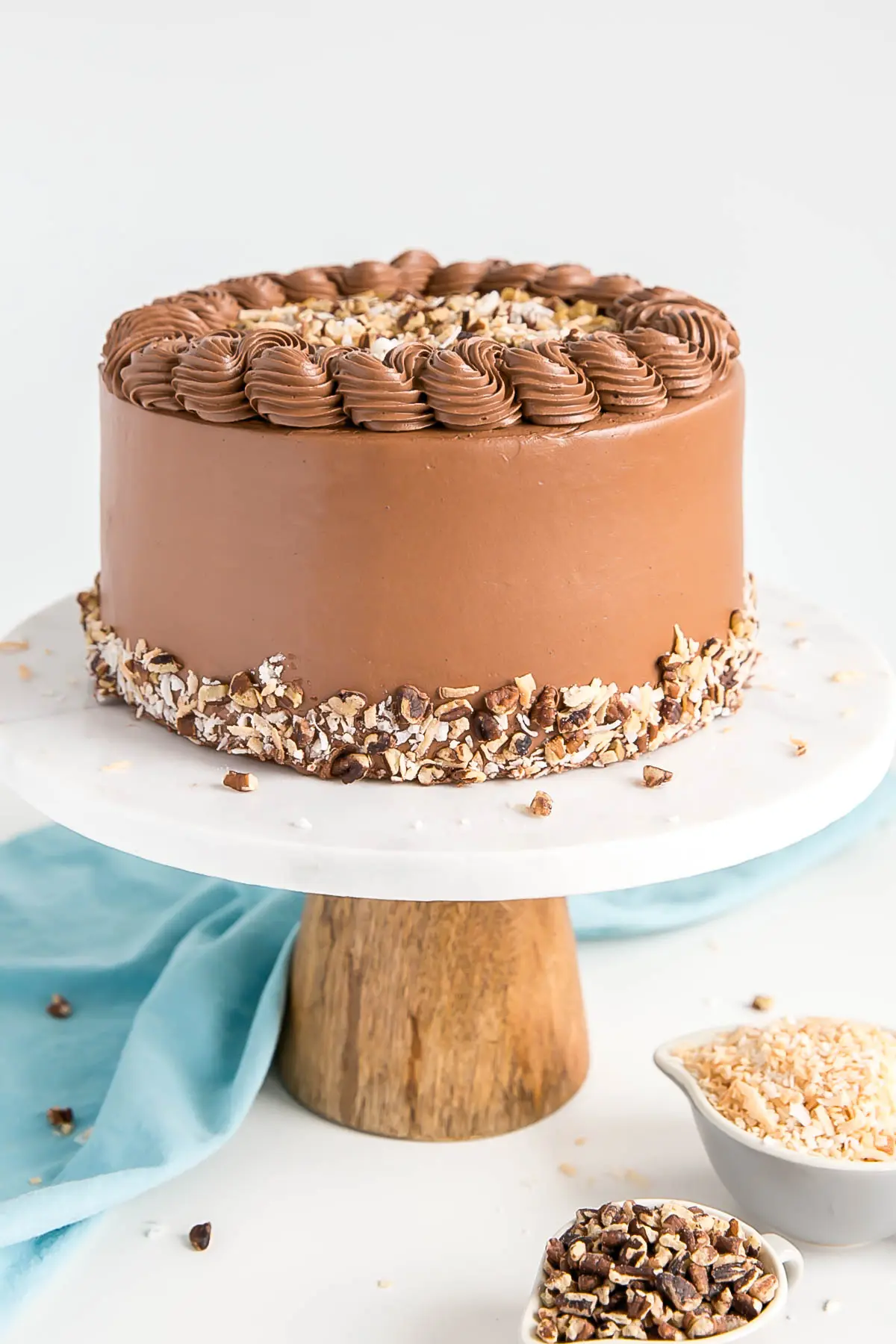 This Classic German Chocolate Cake combines rich chocolate cake layers with a sweet coconut pecan filling and a dreamy chocolate buttercream. | livforcake.com Profile shot of the cake with chocolate buttercream and chopped pecans along the bototm.