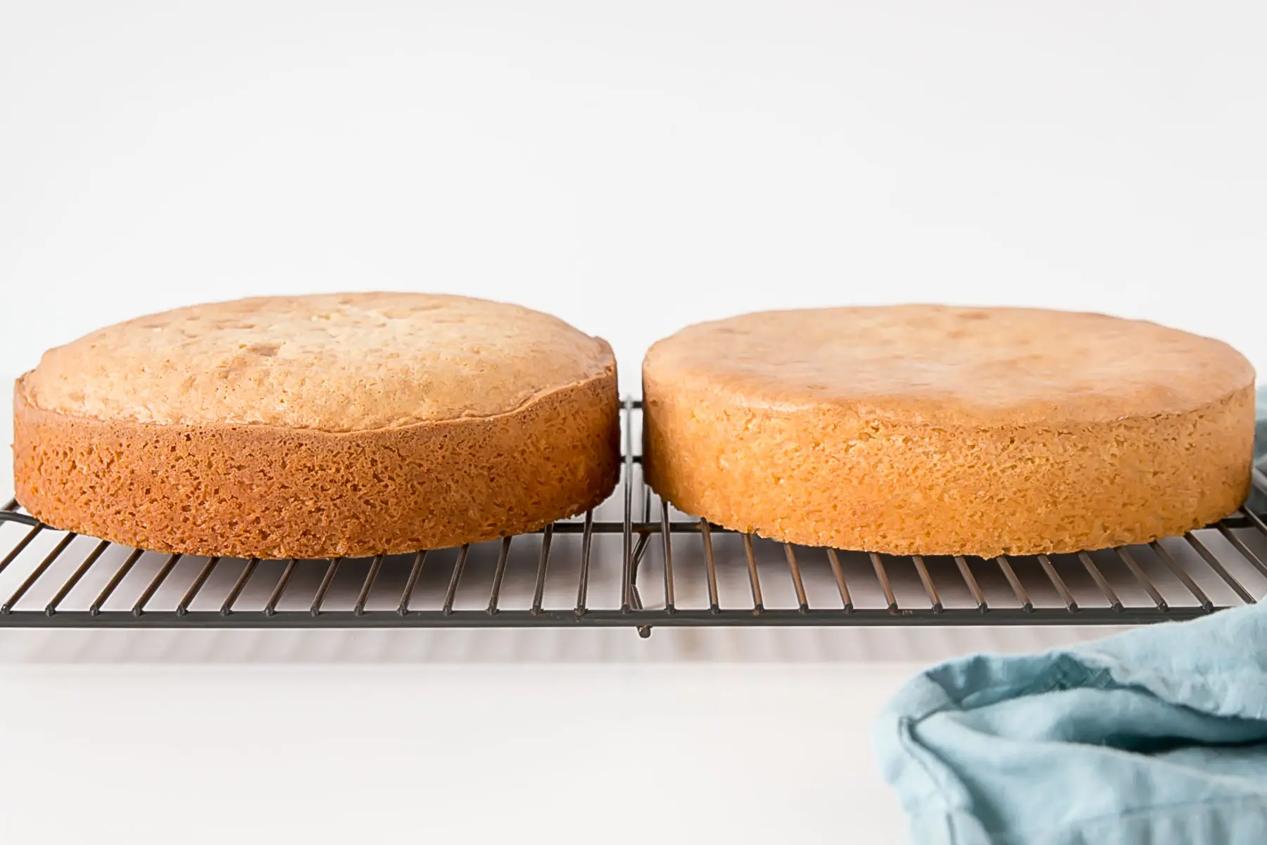 Learn how to bake flat cakes every single time! A simple tutorial on how to make sure your cakes come out nice and flat straight out of the oven. | livforcake.com Side-by-side shot of baked cakes on a cooling rack, one that is domed.