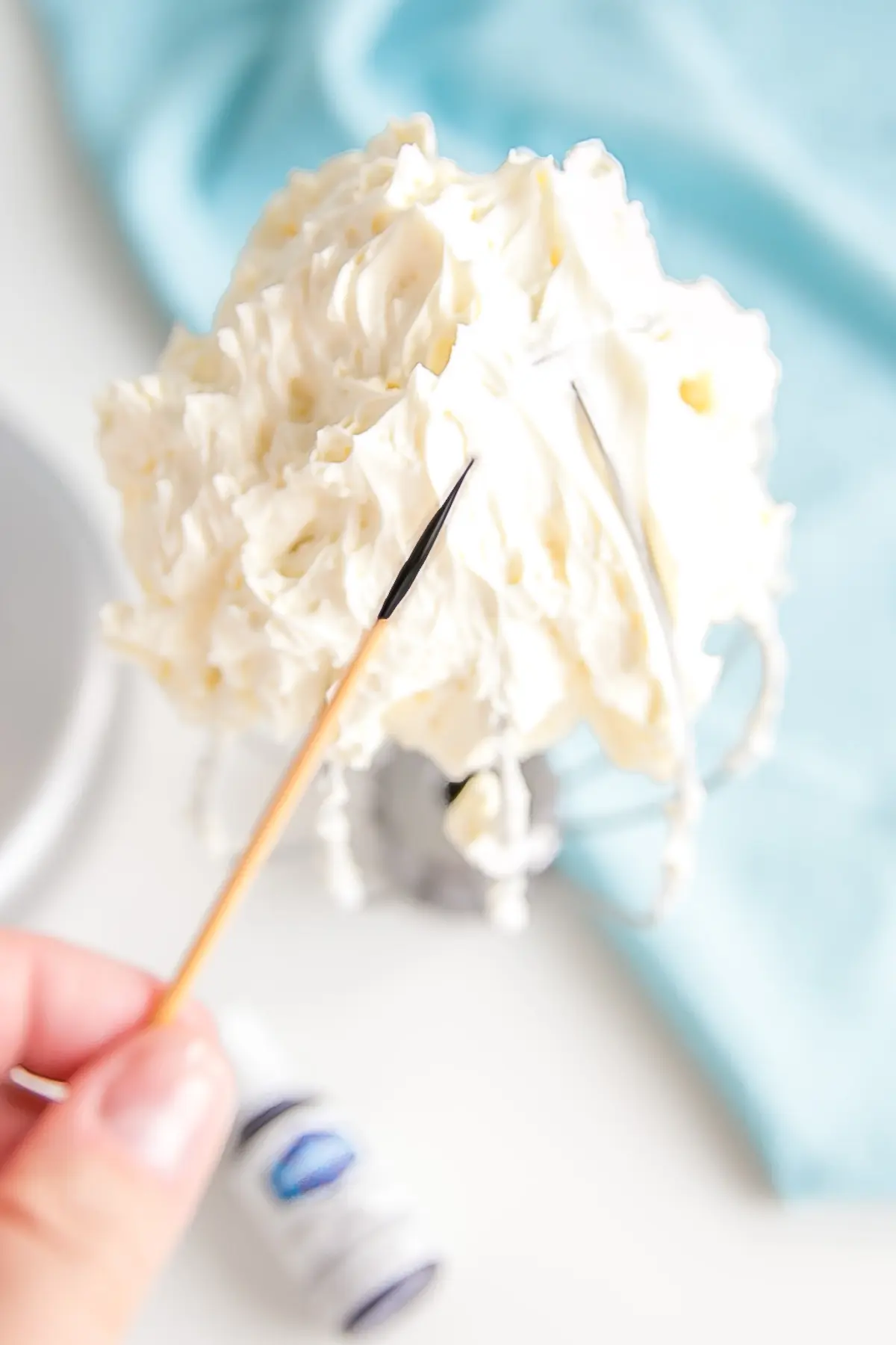 Learn how to make buttercream white with these simple tips & tricks! Perfect for wedding cakes and when you need a white buttercream base to start from. | livforcake.com Showing a toothpick dipped in violet color gel.