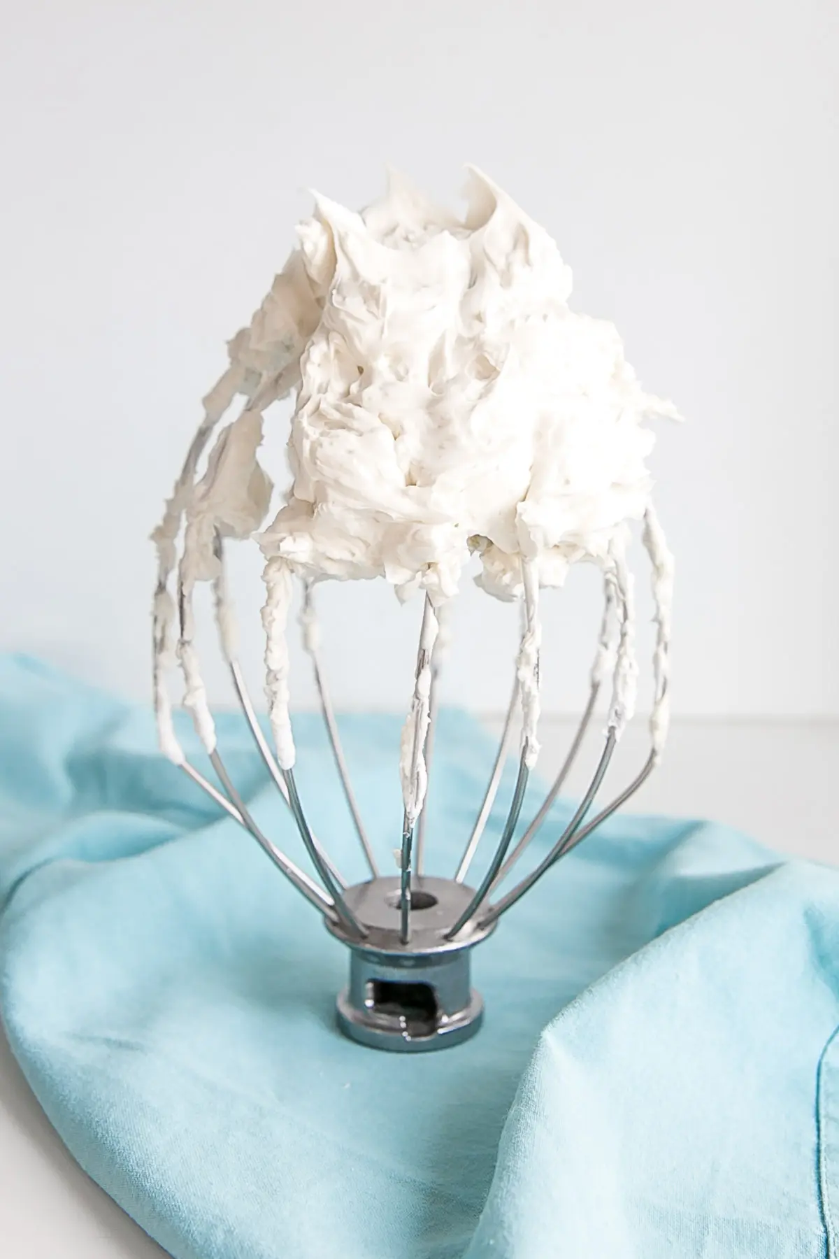 Learn how to make buttercream white with these simple tips & tricks! Perfect for wedding cakes and when you need a white buttercream base to start from. | livforcake.com White buttercream on a stand mixer whisk on a blue cloth.