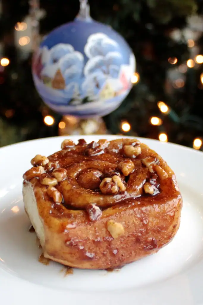 This easy overnight cinnamon rolls recipe is a huge time saver! Make them in advance and pop them in the oven on Christmas morning. | livforcake.com Cinnamon roll on a plate with ornament behind.