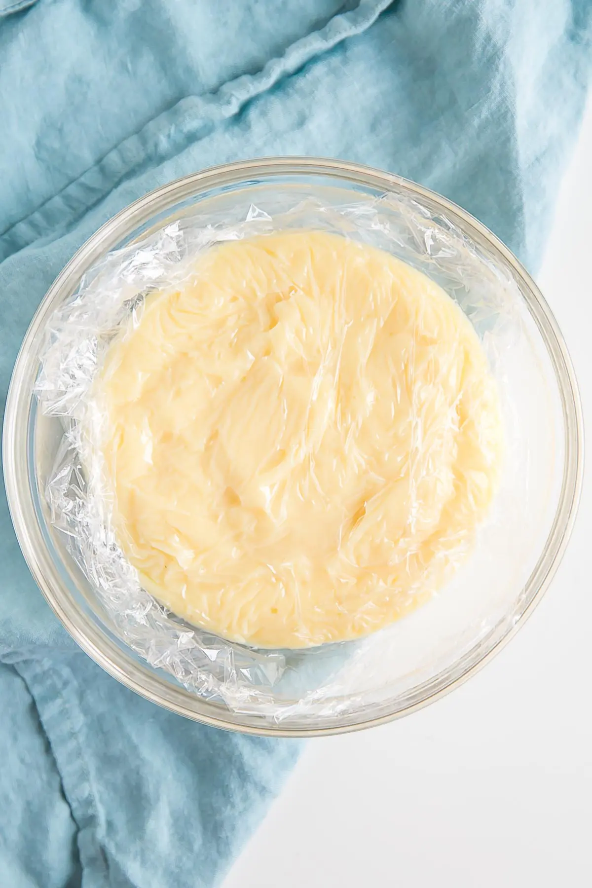 This easy Pastry Cream (Creme Patissiere) recipe is simple and delicious. A rich and creamy vanilla custard you can use in a variety of decadent desserts. | livforcake.com Creme Patissiere in a bowl with plastic wrap directly on top.
