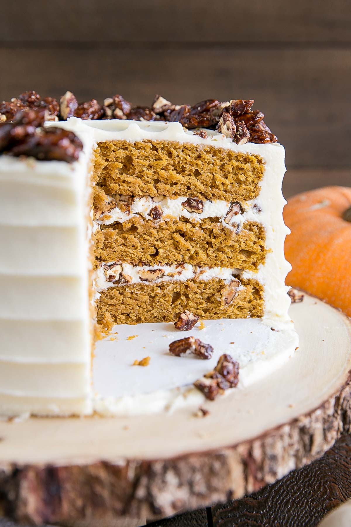 This pumpkin cake is perfect for Fall! Moist and delicious pumpkin cake layers with a tangy cream cheese frosting and crunchy candied pecans. | livforcake.com Cross-section of the cake showing the layers and the candied pecans.