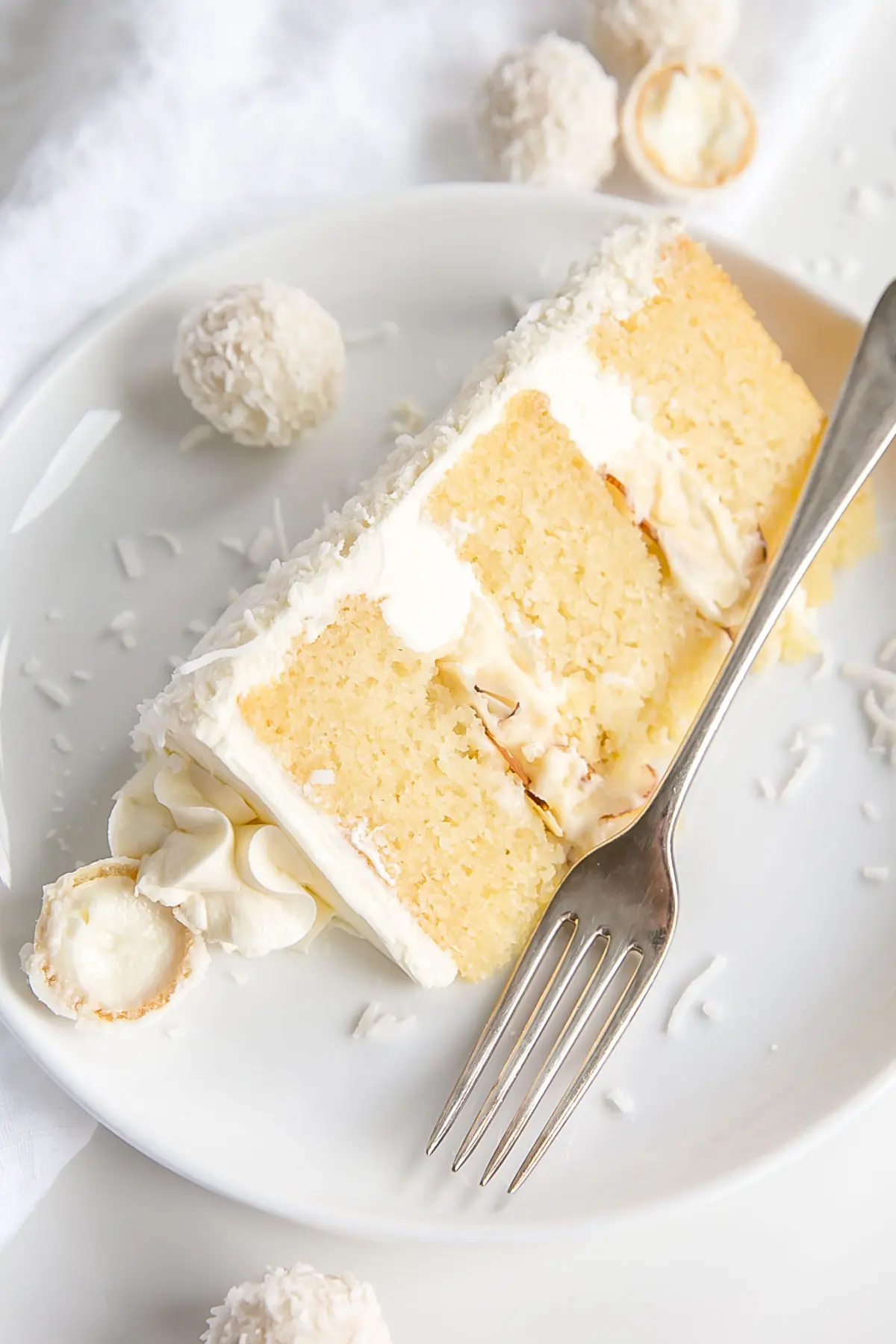 This Raffaello Cake is a coconut lovers dream! Layers of moist and tender almond cake, coconut custard, and coconut Swiss meringue buttercream! | livforcake.com Slice of Raffaello Cake on a plate.