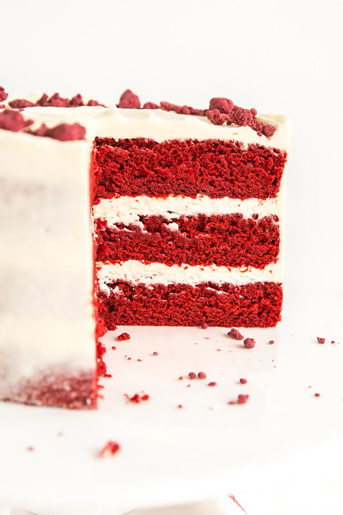 Classic Red Velvet Cake! Tender red cake layers with a hint of chocolate paired with a tangy cream cheese frosting and a red velvet crumble. | livforcake.com Angled cross-section of the cake.