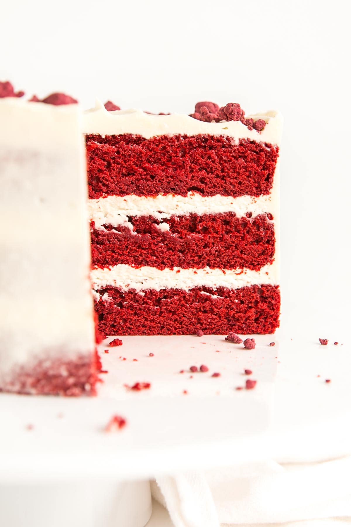 Classic Red Velvet Cake! Tender red cake layers with a hint of chocolate paired with a tangy cream cheese frosting and a red velvet crumble. | livforcake.com Cross section of cake showing three red velvet layers.