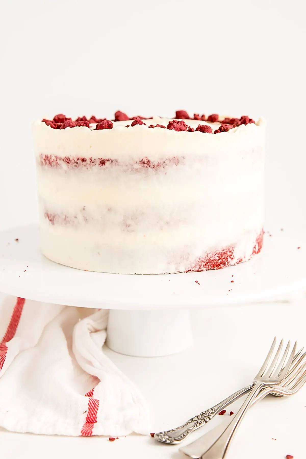 Classic Red Velvet Cake! Tender red cake layers with a hint of chocolate paired with a tangy cream cheese frosting and a red velvet crumble. | livforcake.com Three layer cake on a cake stand.