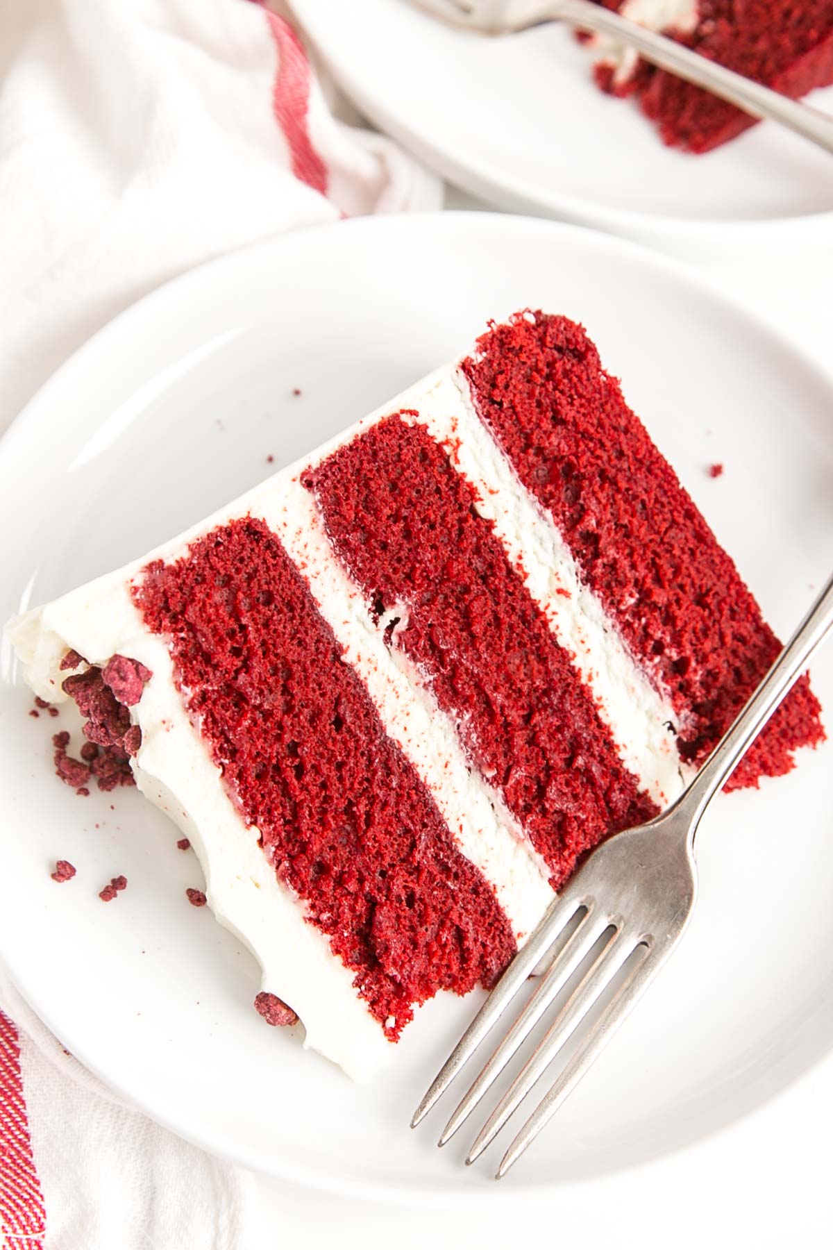 Classic Red Velvet Cake! Tender red cake layers with a hint of chocolate paired with a tangy cream cheese frosting and a red velvet crumble. | livforcake.com Slice of red velvet cake on a plate.