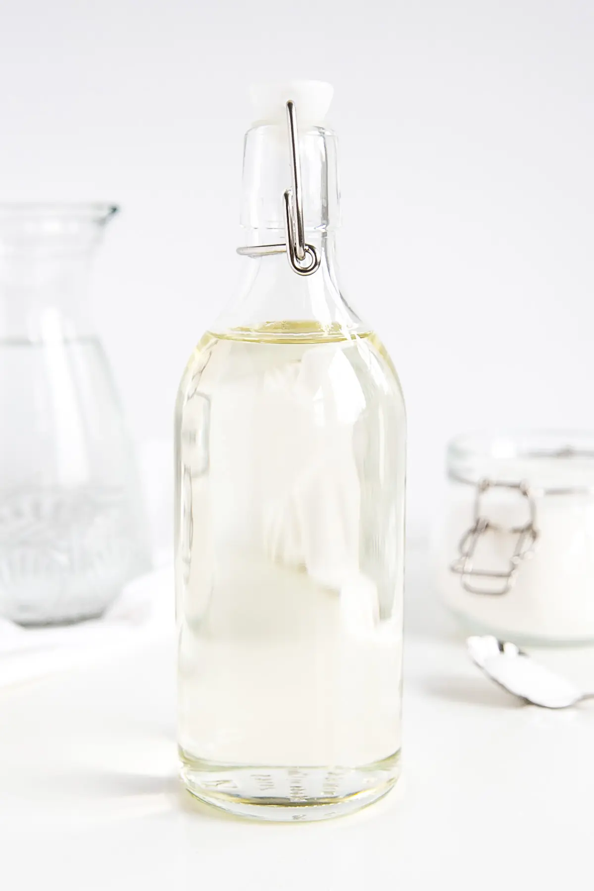 Make simple syrup at home with this quick and easy recipe! The perfect addition to your cakes, cocktails, and iced beverages. | livforcake.com A bottle of homemade simple syrup -- sugar and water in the background.