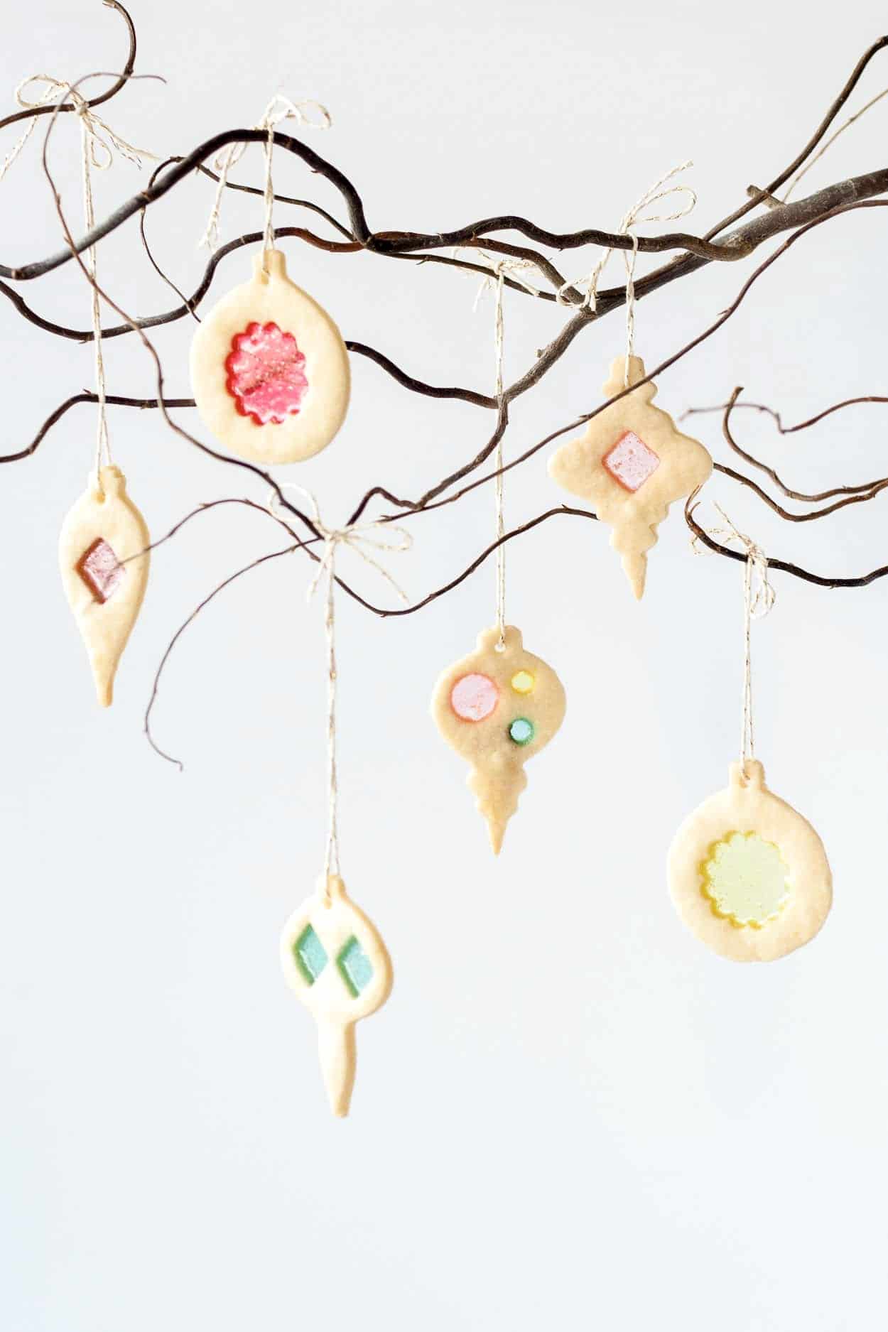 Learn how to make stunning stained glass cookies with this detailed tutorial! Perfect for holiday cookie exchanges or hanging on your tree. | livforcake.com Stained glass cookie ornaments hanging from a tree branch.