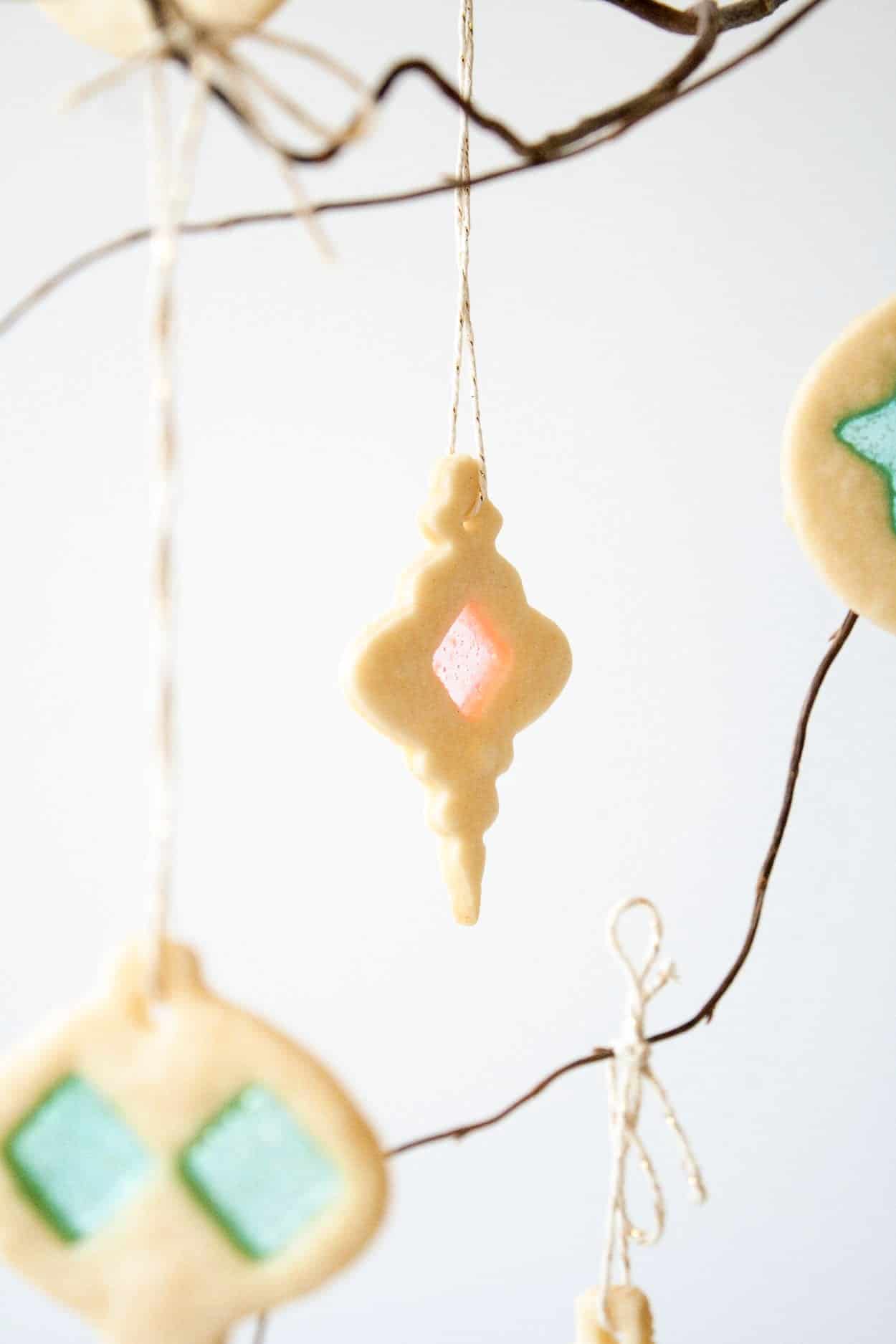 Learn how to make stunning stained glass cookies with this detailed tutorial! Perfect for holiday cookie exchanges or hanging on your tree. | livforcake.com Close up of a stained glass cookie hanging from a branch.