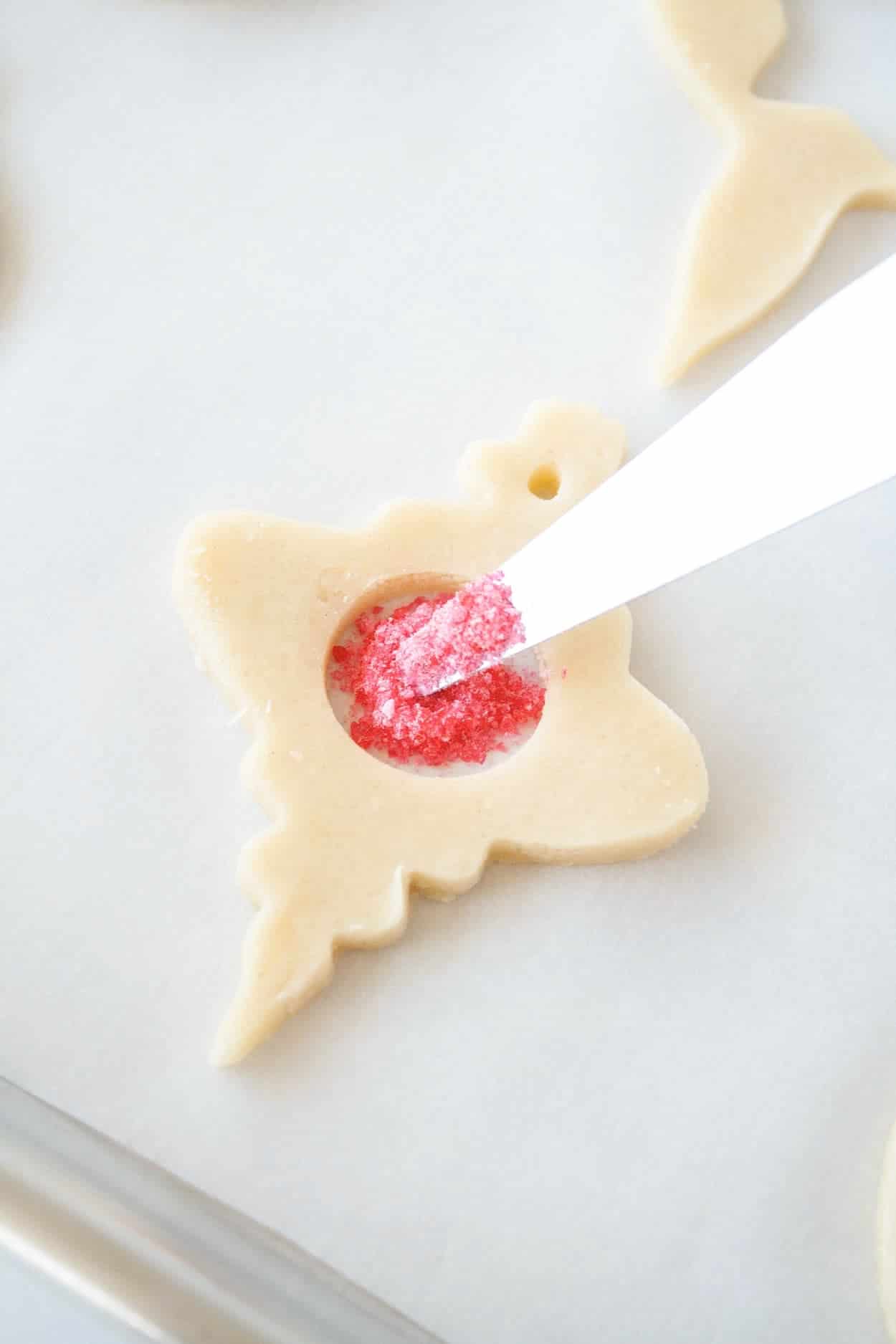 Learn how to make stunning stained glass cookies with this detailed tutorial! Perfect for holiday cookie exchanges or hanging on your tree. | livforcake.com Cut out cookie being filled with sanding sugar