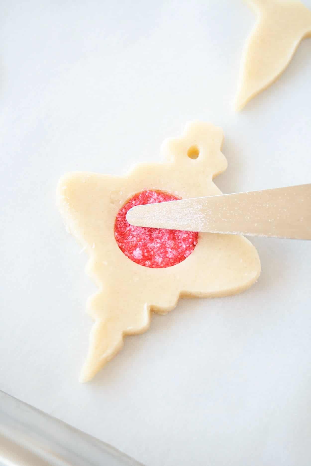 Learn how to make stunning stained glass cookies with this detailed tutorial! Perfect for holiday cookie exchanges or hanging on your tree. | livforcake.com Stained Glass Cookie filled with red sanding sugar before baking.