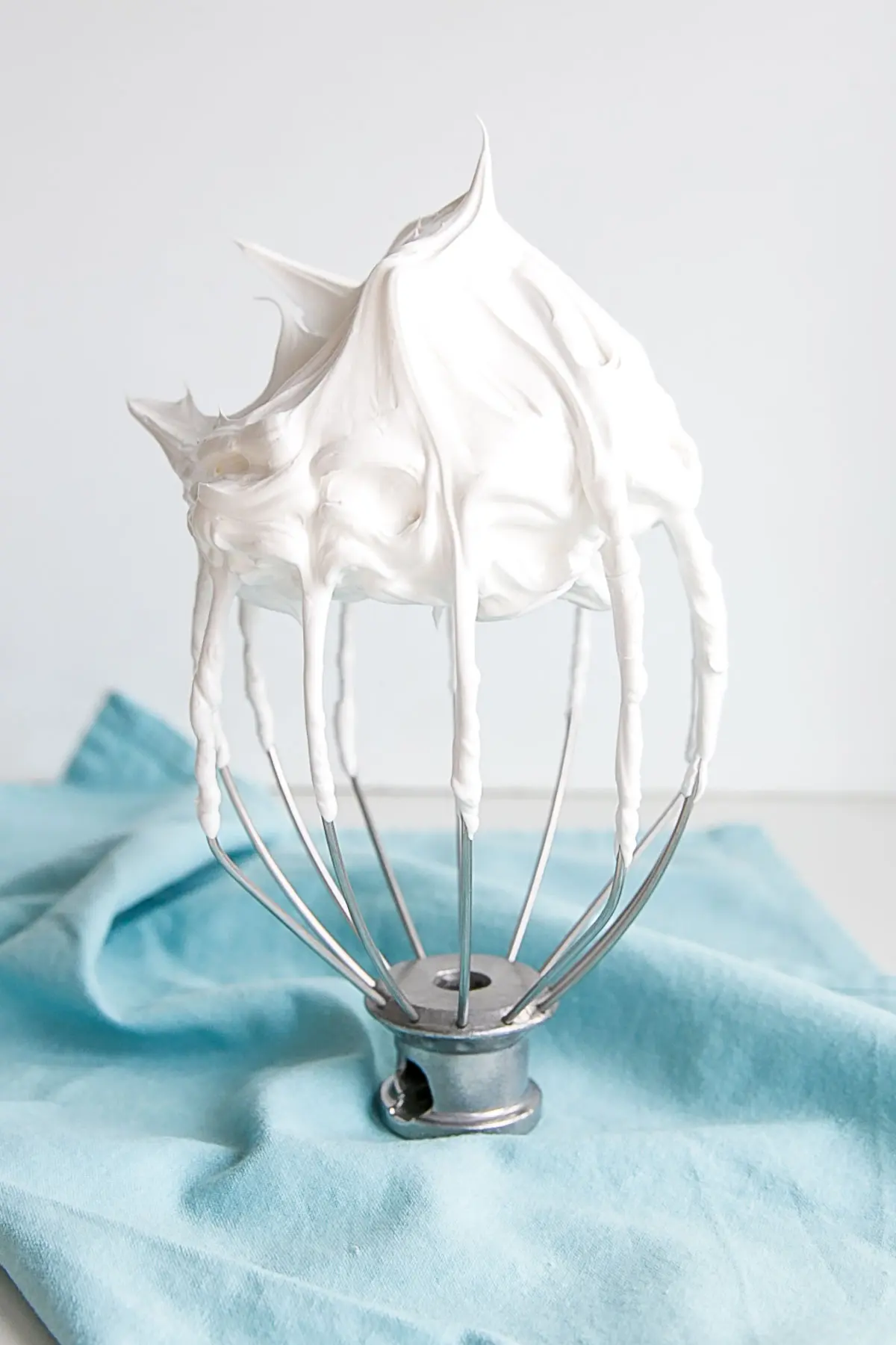 This tutorial on how to make Swiss Meringue buttercream is the only resource you'll need to make the smoothest, silkiest frosting! | livforcake.com Picture of a stiff peak meringue on a stand mixer whisk.