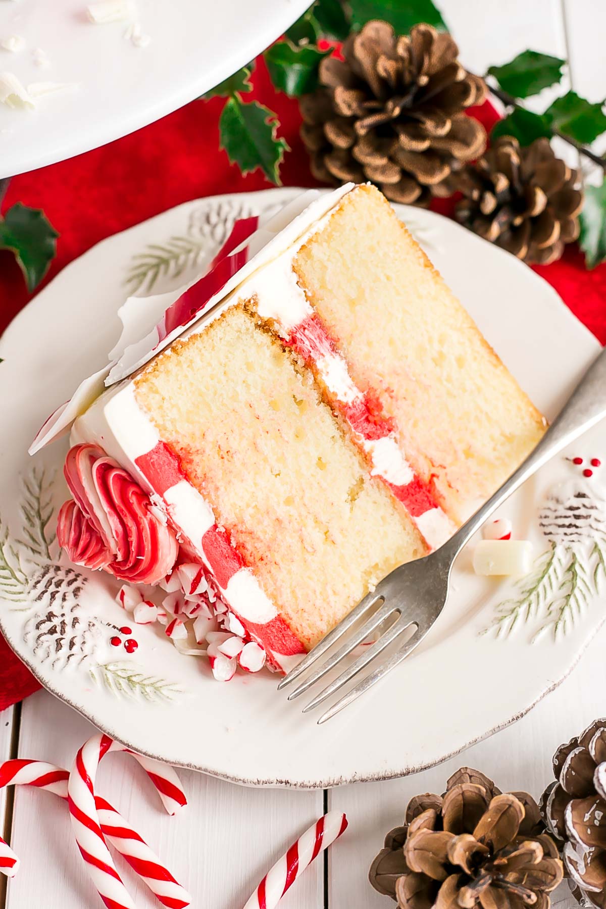 This White Chocolate Candy Cane Cake is the perfect addition to your holiday celebrations! | livforcake.com Slice of cake on a plate showing striped buttercream.